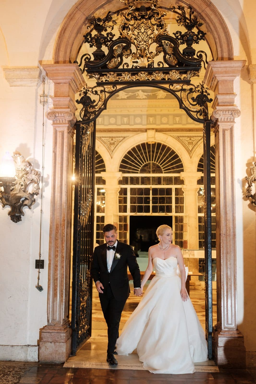 A bride and groom walking through a sunlit venue doorway