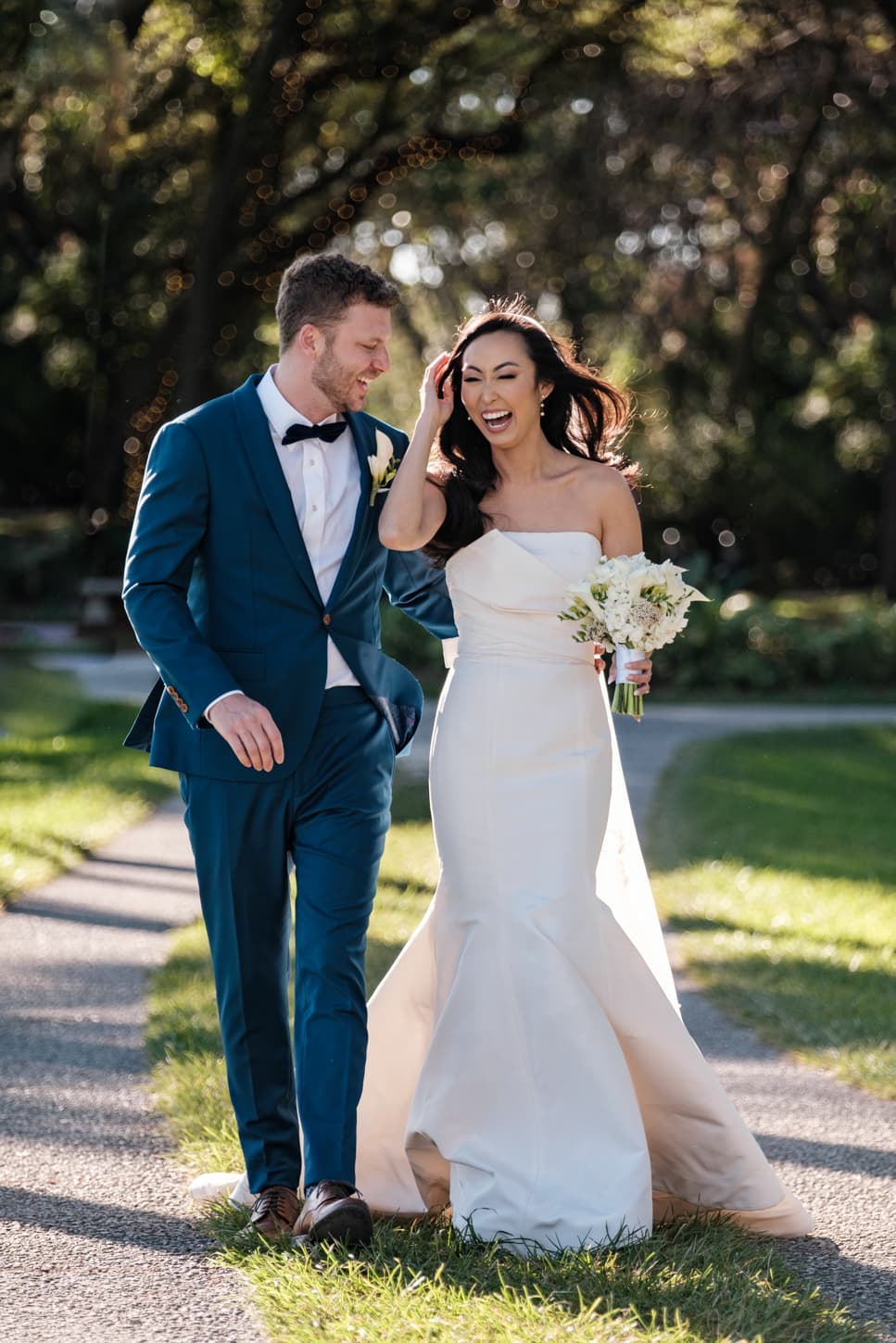 A bride in a white gown and a groom in a blue suit standing together on a lawn