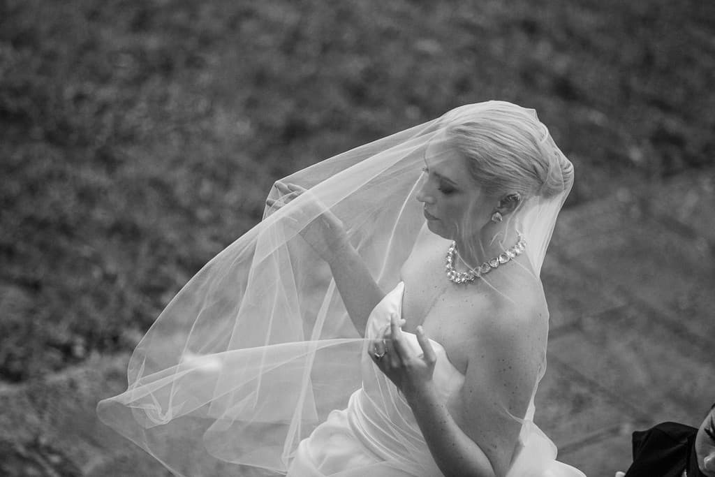 A black and white photograph of a bride in a long veil, looking down