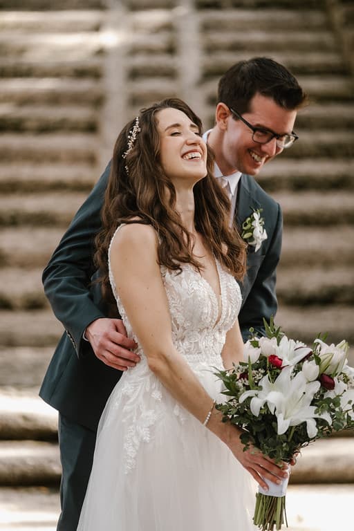 A bride and groom on stone steps, turned toward each other and laughing