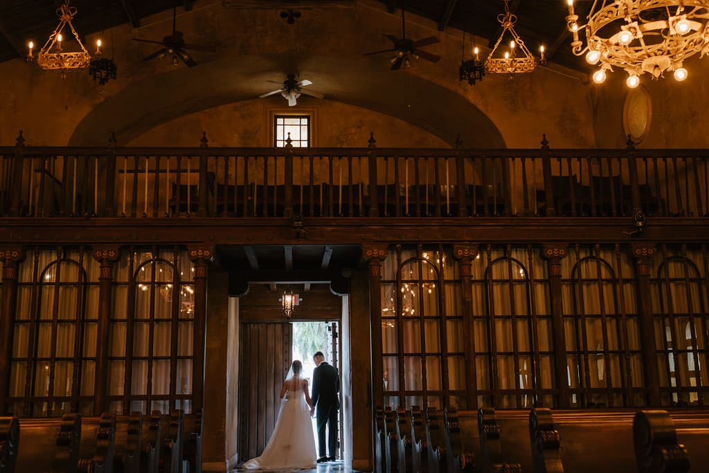 A couple small in the distance of an ornate, lamplit hall
