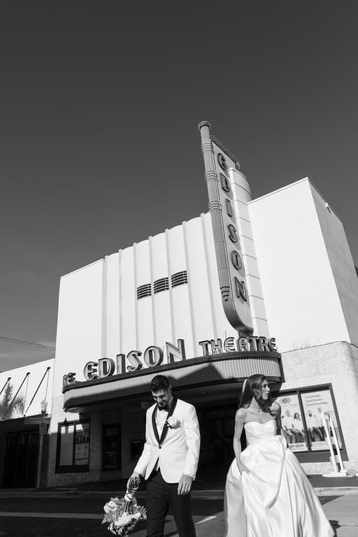 A black and white photograph of a bride and groom in front of a theater marquee