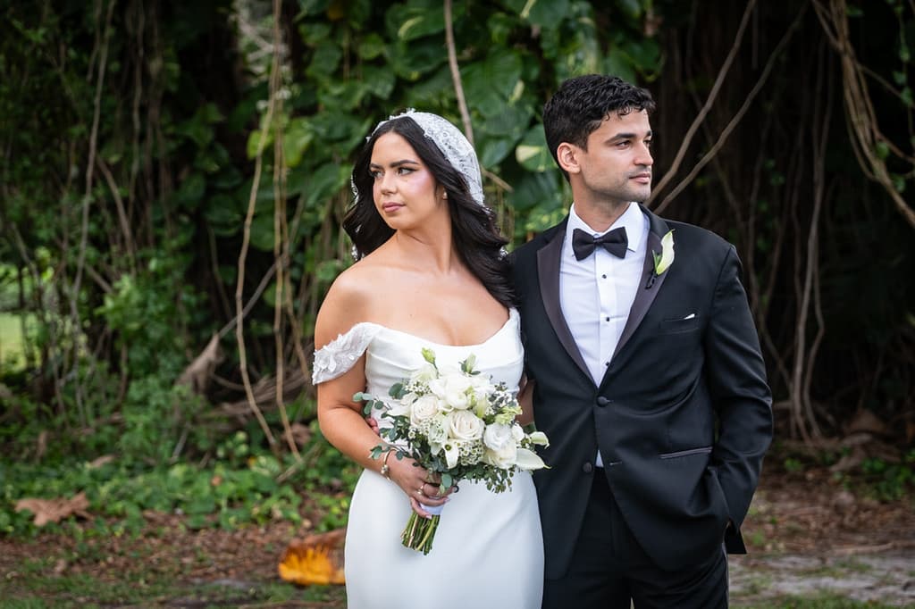 A bride and groom standing in a garden, the bride holding a bouquet