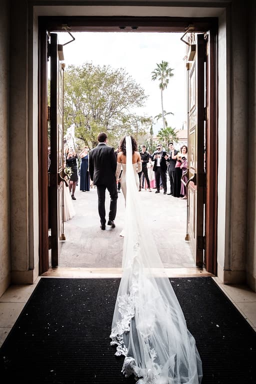 A bride and groom walking away through a doorway, her veil spreading behind them
