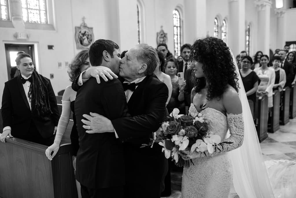 A couple kissing in a church aisle as guests look on