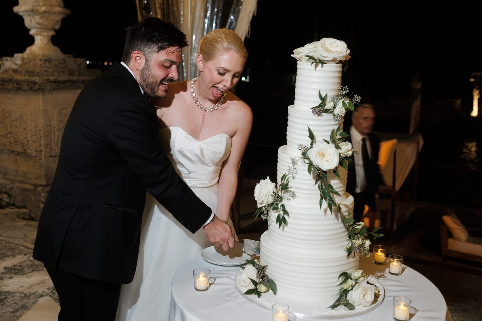 Amy laughing as she and Chris cut a tall white wedding cake at Vizcaya
