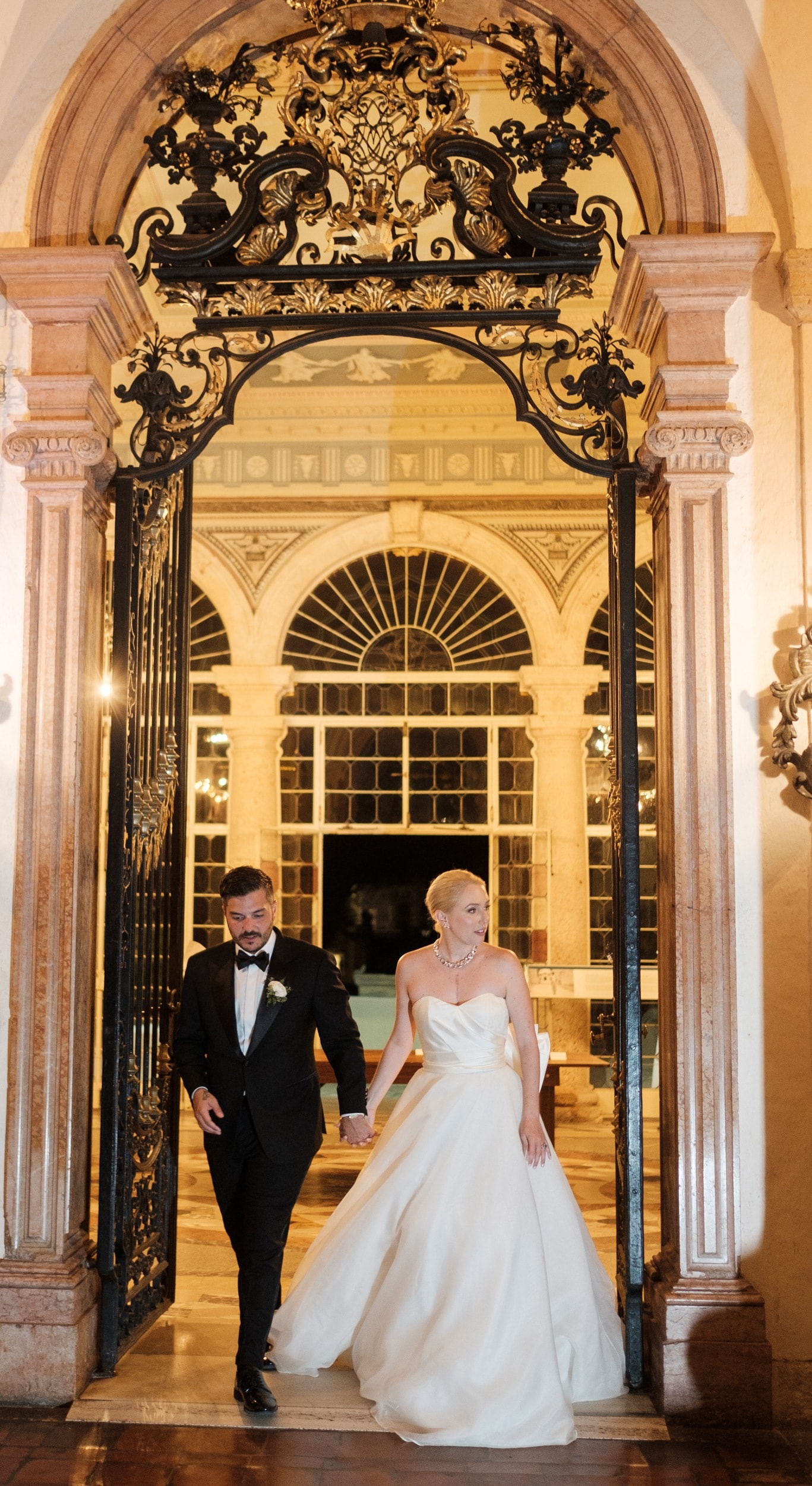 Amy and Christian walking hand in hand through an ornate doorway, looking ahead rather than at the camera